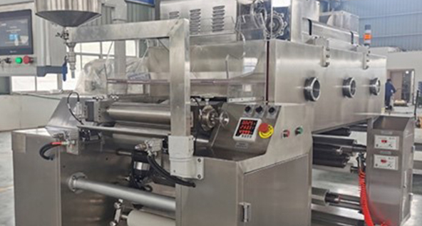 Image of a large industrial machine used for manufacturing, likely involved in the production of fast action oral solid dosage forms, featuring multiple rollers, control panels, and components for processing materials.